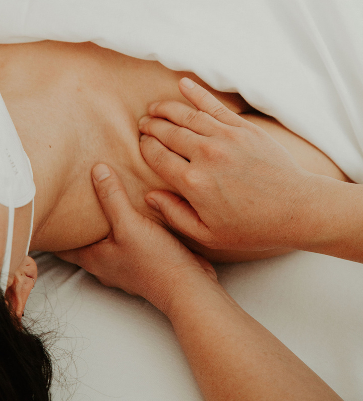 Close up photo of a client laying on their back, just the right shoulder is exposed. The massage therapist's hands smoothly press below the clavicle while lifting the trapezius muscle from below.